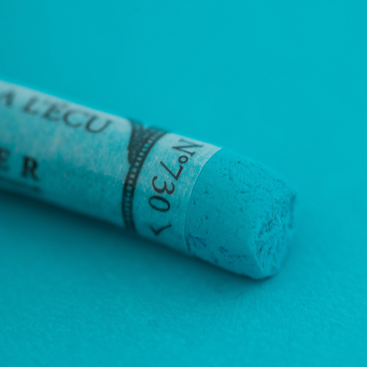 A close-up of a green Sennelier extra soft pastel. on the same coloured background, with the colour information printed on the paper wrap.