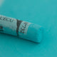 A close-up of a green Sennelier extra soft pastel. on the same coloured background, with the colour information printed on the paper wrap.