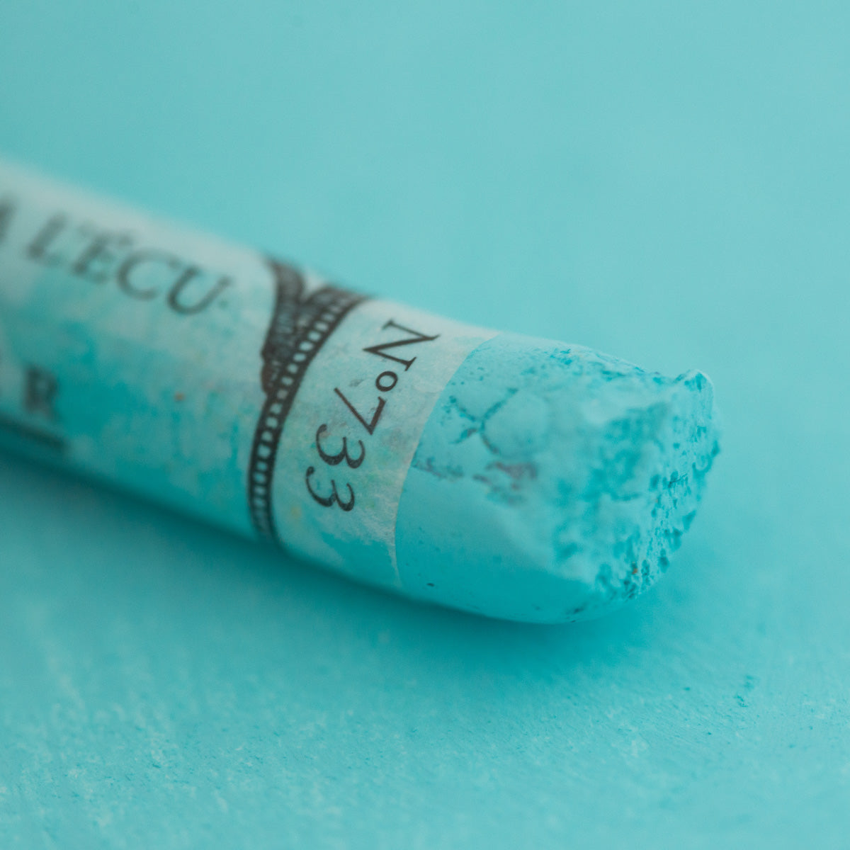 A close-up of a light green Sennelier extra soft pastel. on the same coloured background, with the colour information printed on the paper wrap.