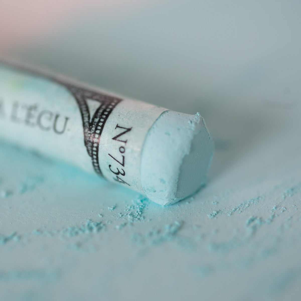 A close-up of a white Sennelier extra soft pastel. on the same coloured background, with the colour information printed on the paper wrap.