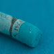 A close-up of a blue/green Sennelier extra soft pastel. on the same coloured background, with the colour information printed on the paper wrap.