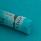 A close-up of a blue/green Sennelier extra soft pastel. on the same coloured background, with the colour information printed on the paper wrap.