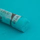A close-up of a blue/green Sennelier extra soft pastel. on the same coloured background, with the colour information printed on the paper wrap.