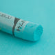 A close-up of a blue/green Sennelier extra soft pastel. on the same coloured background, with the colour information printed on the paper wrap.