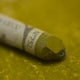 A close-up of a green Sennelier extra soft pastel, on the same coloured background, with the colour information printed on the paper wrap.