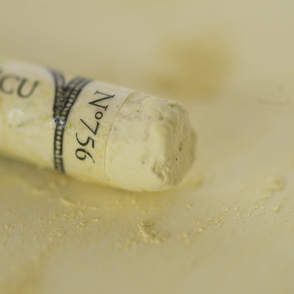 A close-up of a white Sennelier extra soft pastel, on the same coloured background, with the colour information printed on the paper wrap.