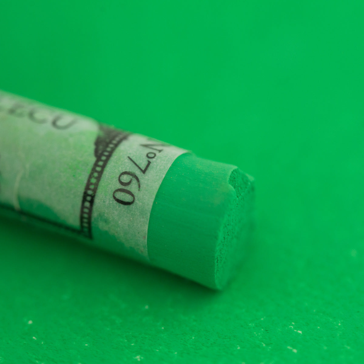 A close-up of a bright green Sennelier extra soft pastel. on the same coloured background, with the colour information printed on the paper wrap.
