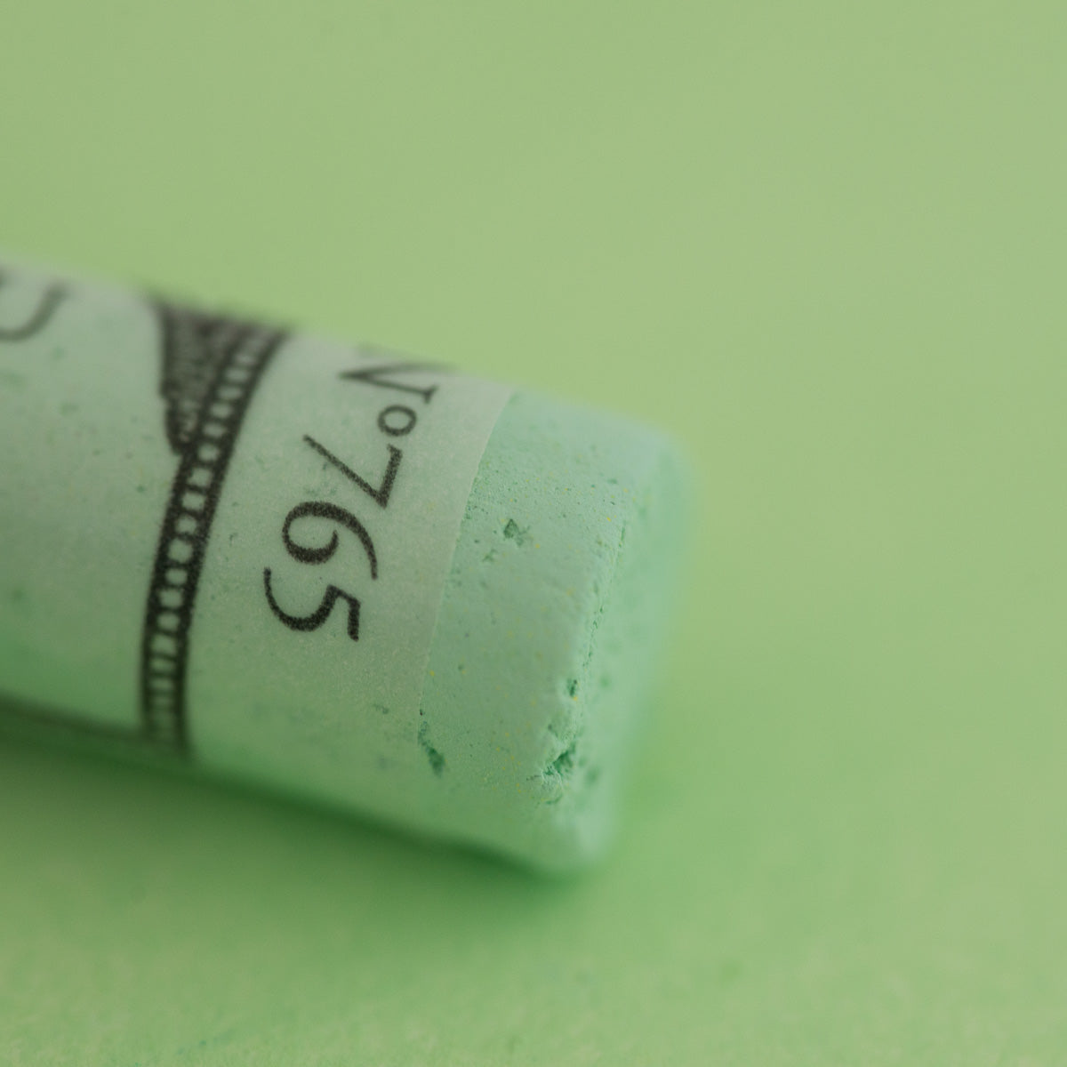 A close-up of a light green Sennelier extra soft pastel. on the same coloured background, with the colour information printed on the paper wrap.