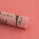 A close-up of a pale red Sennelier extra soft pastel on the same coloured background, with the colour information printed on the paper wrap.