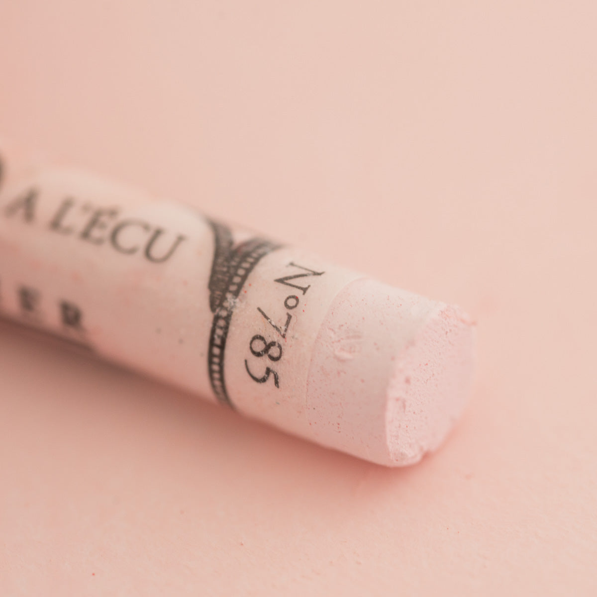 A close-up of a white Sennelier extra soft pastel on the same coloured background, with the colour information printed on the paper wrap.