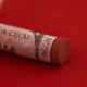 A close-up of a dark red Sennelier extra soft pastel. on the same coloured background, with the colour information printed on the paper wrap.