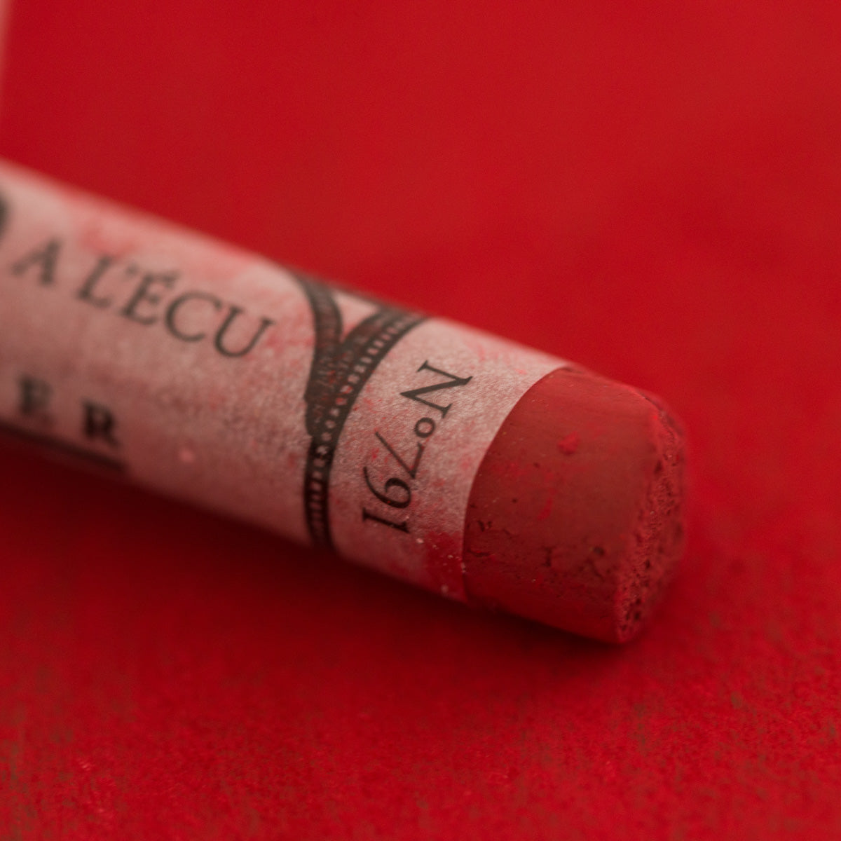 A close-up of a deep red Sennelier extra soft pastel. on the same coloured background, with the colour information printed on the paper wrap.