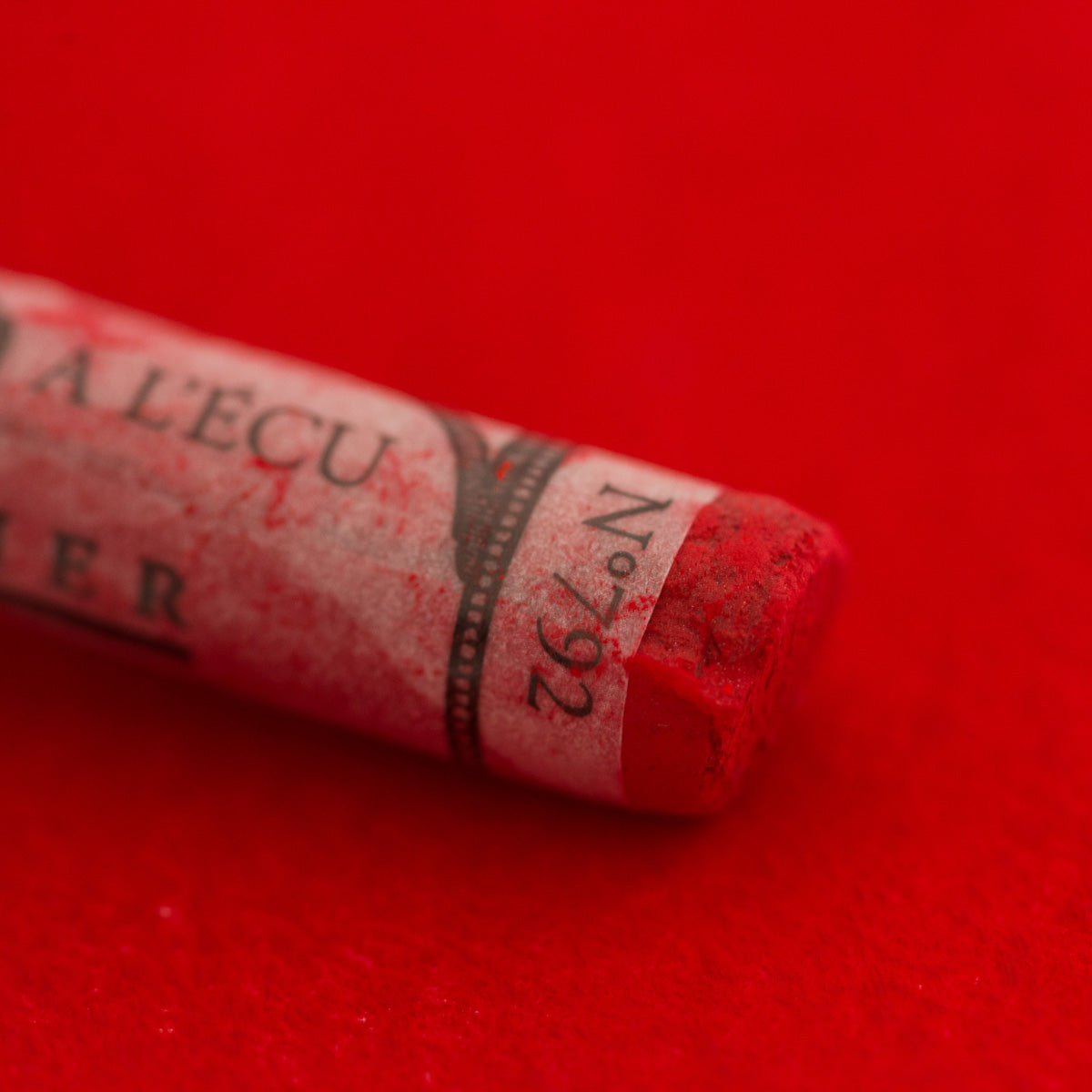 A close-up of a bright red Sennelier extra soft pastel. on the same coloured background, with the colour information printed on the paper wrap.