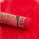 A close-up of a red Sennelier extra soft pastel. on the same coloured background, with the colour information printed on the paper wrap.