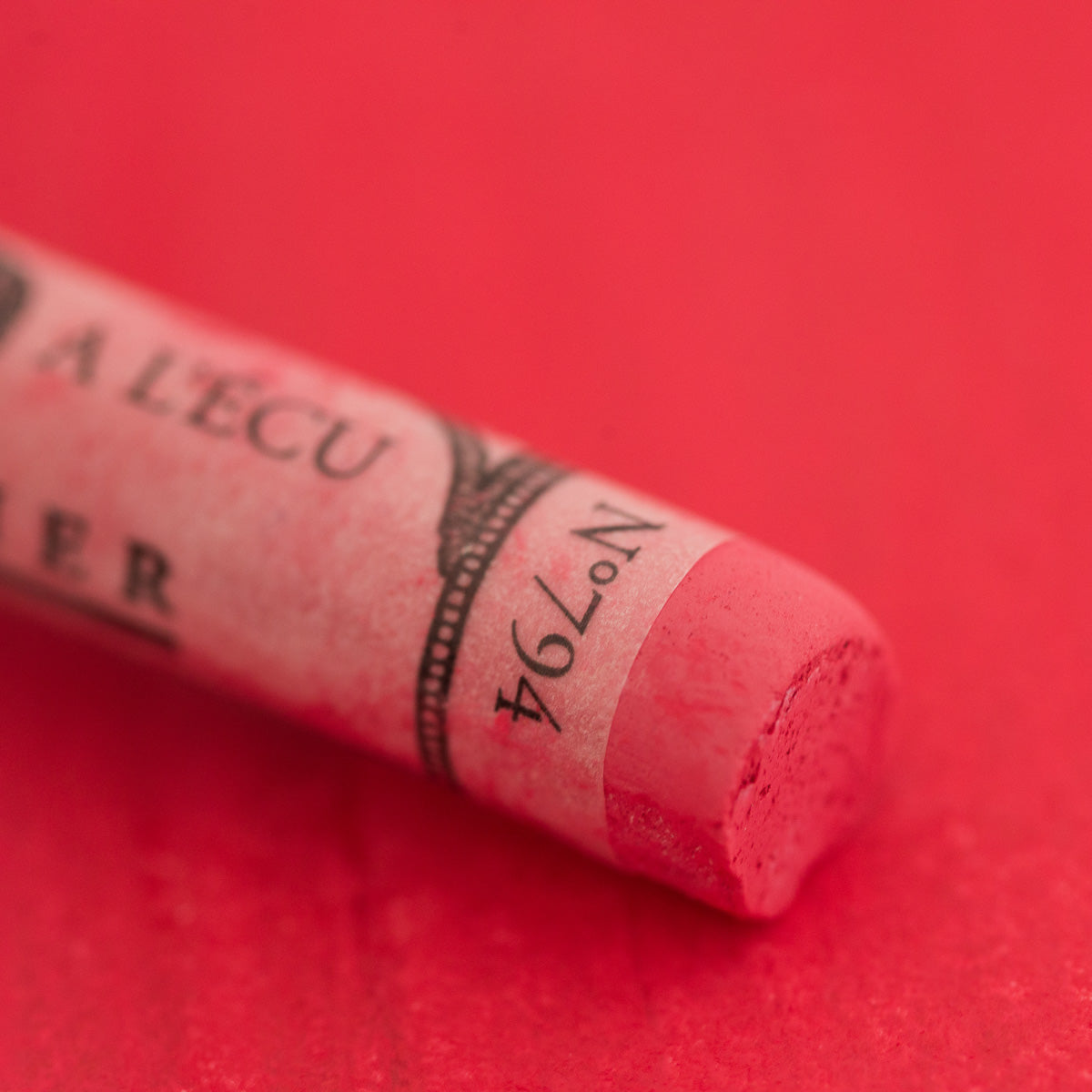 A close-up of a red Sennelier extra soft pastel. on the same coloured background, with the colour information printed on the paper wrap.