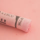 A close-up of a pale red Sennelier extra soft pastel. on the same coloured background, with the colour information printed on the paper wrap.