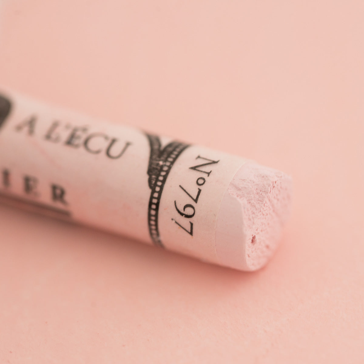 A close-up of a white Sennelier extra soft pastel on the same coloured background, with the colour information printed on the paper wrap.