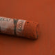 A close-up of a brown Sennelier extra soft pastel with the colour information printed on the paper wrap.
