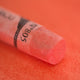 A close-up of an iridescent Sennelier extra soft pastel. on the same coloured background, with the colour information printed on the paper wrap.