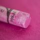 A close-up of an iridescent pink Sennelier extra soft pastel. on the same coloured background, with the colour information printed on the paper wrap.