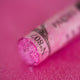 A close-up of an iridescent pink Sennelier extra soft pastel. on the same coloured background, with the colour information printed on the paper wrap.