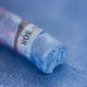 A close-up of an iridescent Sennelier extra soft pastel. on the same coloured background, with the colour information printed on the paper wrap.
