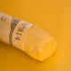 A close-up of an iridescent yellow Sennelier extra soft pastel. on the same coloured background, with the colour information printed on the paper wrap.