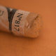 A close-up of an iridescent brown Sennelier extra soft pastel. on the same coloured background, with the colour information printed on the paper wrap.