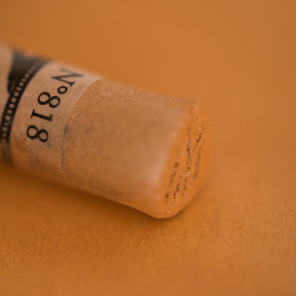 A close-up of an iridescent brown Sennelier extra soft pastel. on the same coloured background, with the colour information printed on the paper wrap.