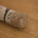 A close-up of an iridescent brown Sennelier extra soft pastel. on the same coloured background, with the colour information printed on the paper wrap.