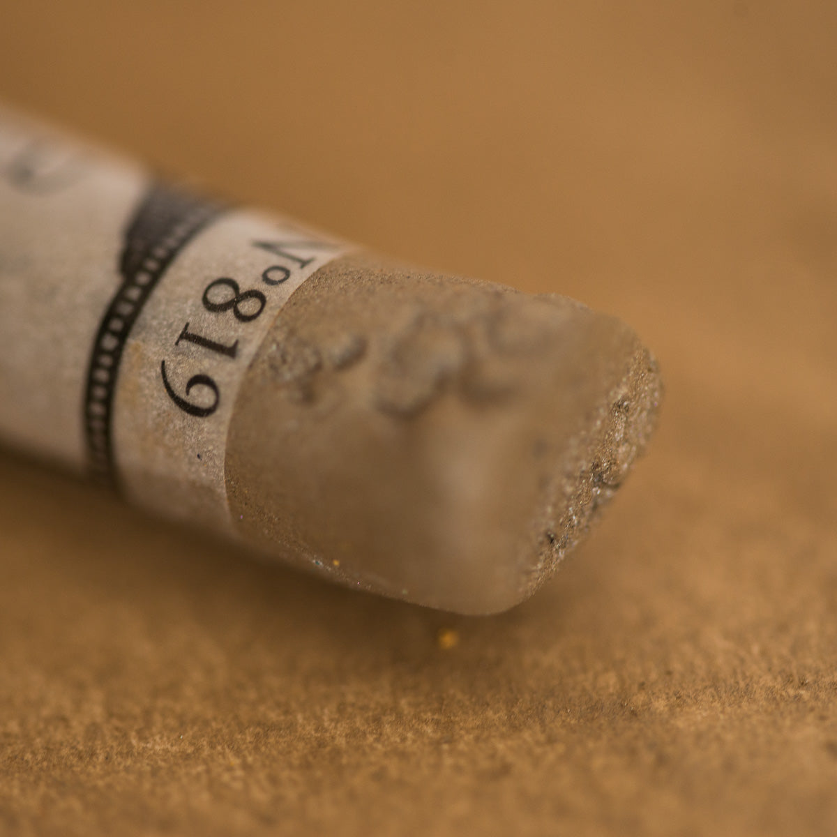 A close-up of an iridescent brown Sennelier extra soft pastel. on the same coloured background, with the colour information printed on the paper wrap.
