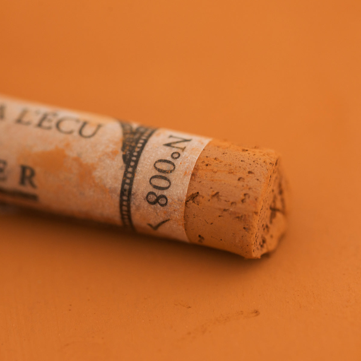 A close-up of a Sennelier extra soft pastel on a brown background with the colour information printed on the paper wrap.