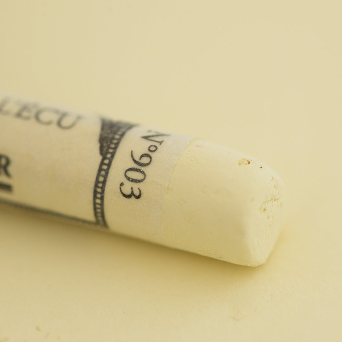 A close-up of a pale yellow Sennelier extra soft pastel. on the same coloured background, with the colour information printed on the paper wrap.