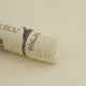 A close-up of a white Sennelier extra soft pastel. on the same coloured background, with the colour information printed on the paper wrap.