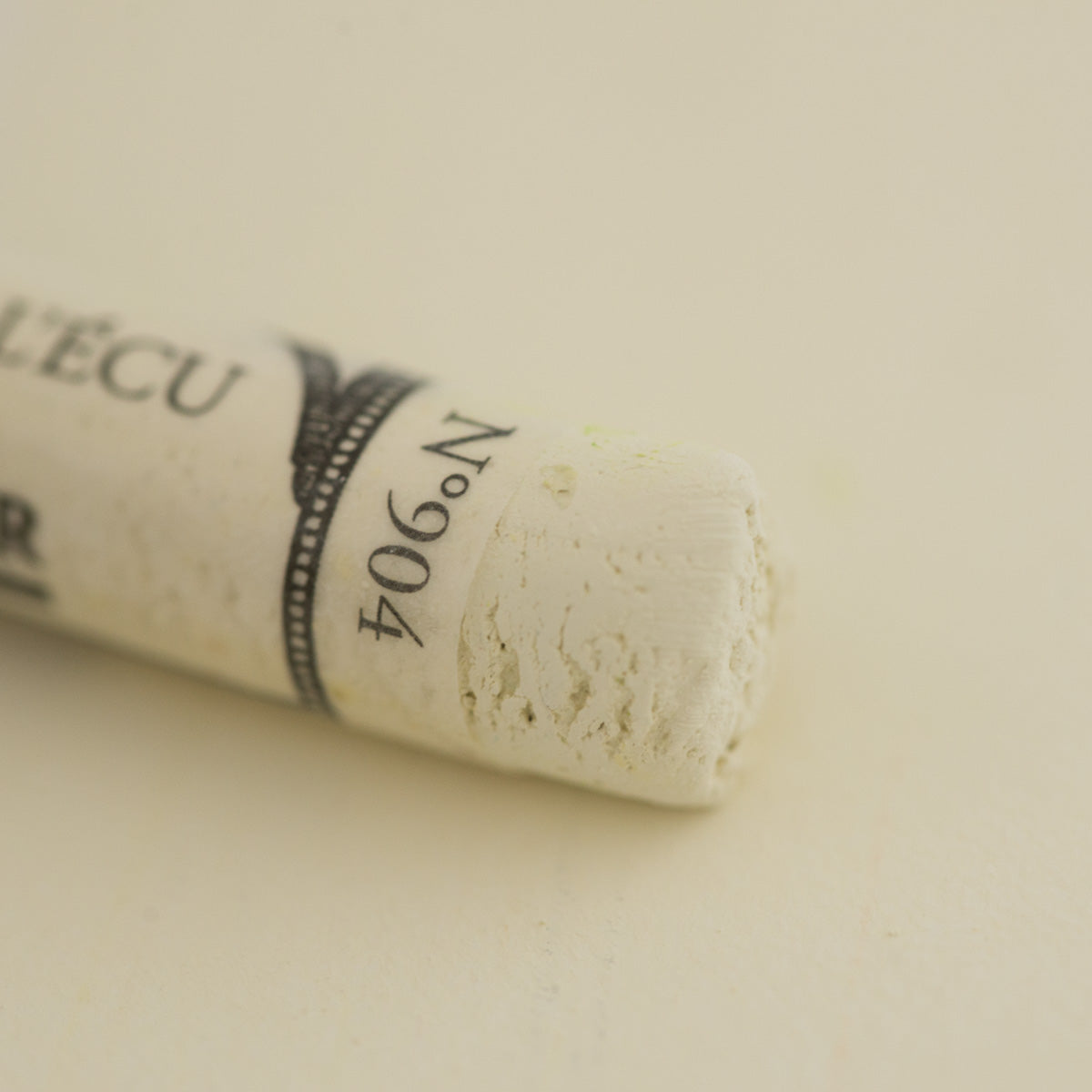 A close-up of a white Sennelier extra soft pastel. on the same coloured background, with the colour information printed on the paper wrap.