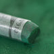 A close-up of a green Sennelier extra soft pastel, on the same coloured background, with the colour information printed on the paper wrap.