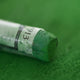 A close-up of a green Sennelier extra soft pastel, on the same coloured background, with the colour information printed on the paper wrap.