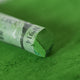 A close-up of a green Sennelier extra soft pastel, on the same coloured background, with the colour information printed on the paper wrap.