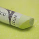 A close-up of a light green Sennelier extra soft pastel, on the same coloured background, with the colour information printed on the paper wrap.