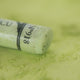 A close-up of a light green Sennelier extra soft pastel, on the same coloured background, with the colour information printed on the paper wrap.