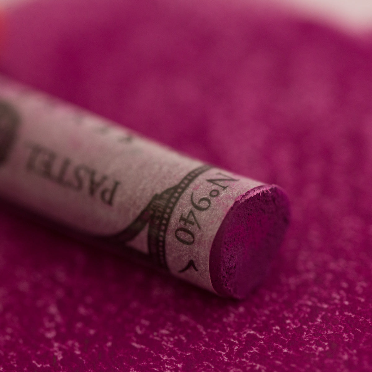 A close-up of a purple Sennelier extra soft pastel. on the same coloured background, with the colour information printed on the paper wrap.