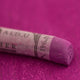 A close-up of a purple Sennelier extra soft pastel. on the same coloured background, with the colour information printed on the paper wrap.