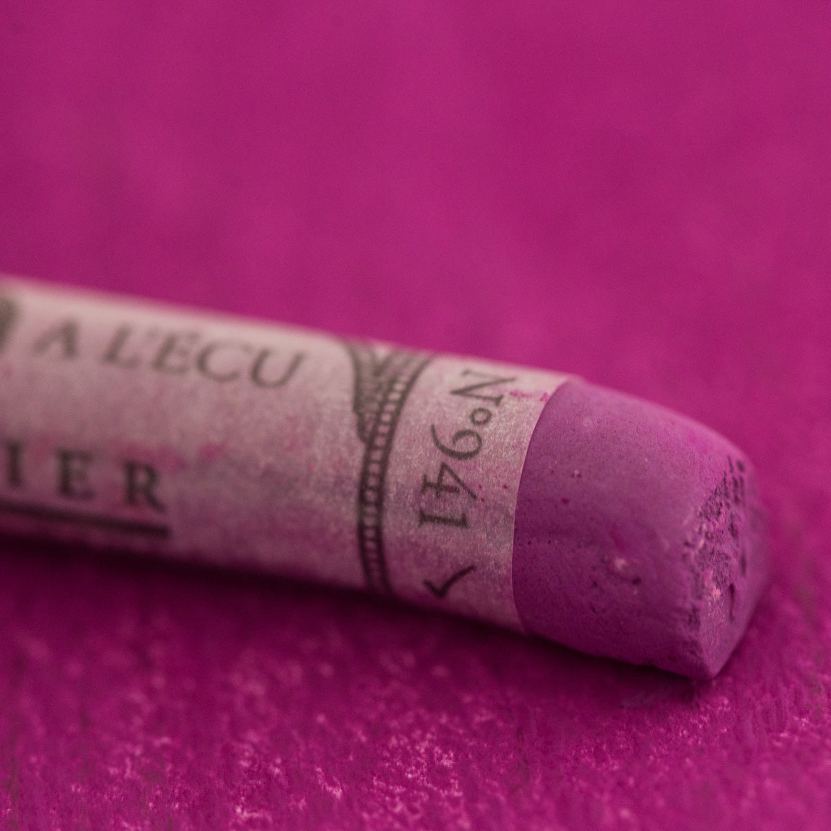 A close-up of a purple Sennelier extra soft pastel. on the same coloured background, with the colour information printed on the paper wrap.