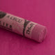 A close-up of a purple Sennelier extra soft pastel. on the same coloured background, with the colour information printed on the paper wrap.