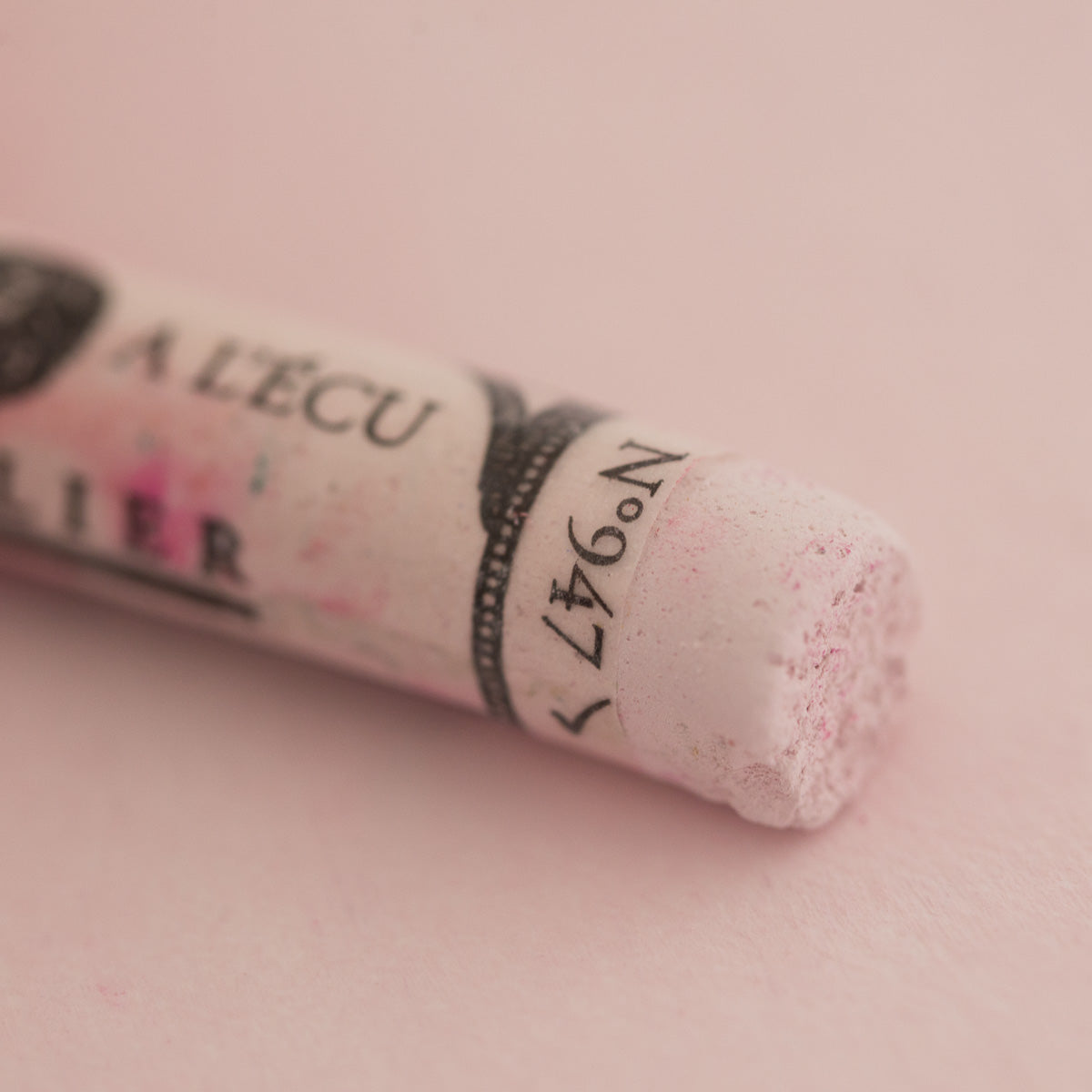 A close-up of a white Sennelier extra soft pastel. on the same coloured background, with the colour information printed on the paper wrap.