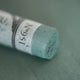 A close-up of a blue-grey Sennelier extra soft pastel. on the same coloured background, with the colour information printed on the paper wrap.