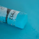 A close-up of a bright blue Sennelier extra soft pastel. on the same coloured background, with the colour information printed on the paper wrap.