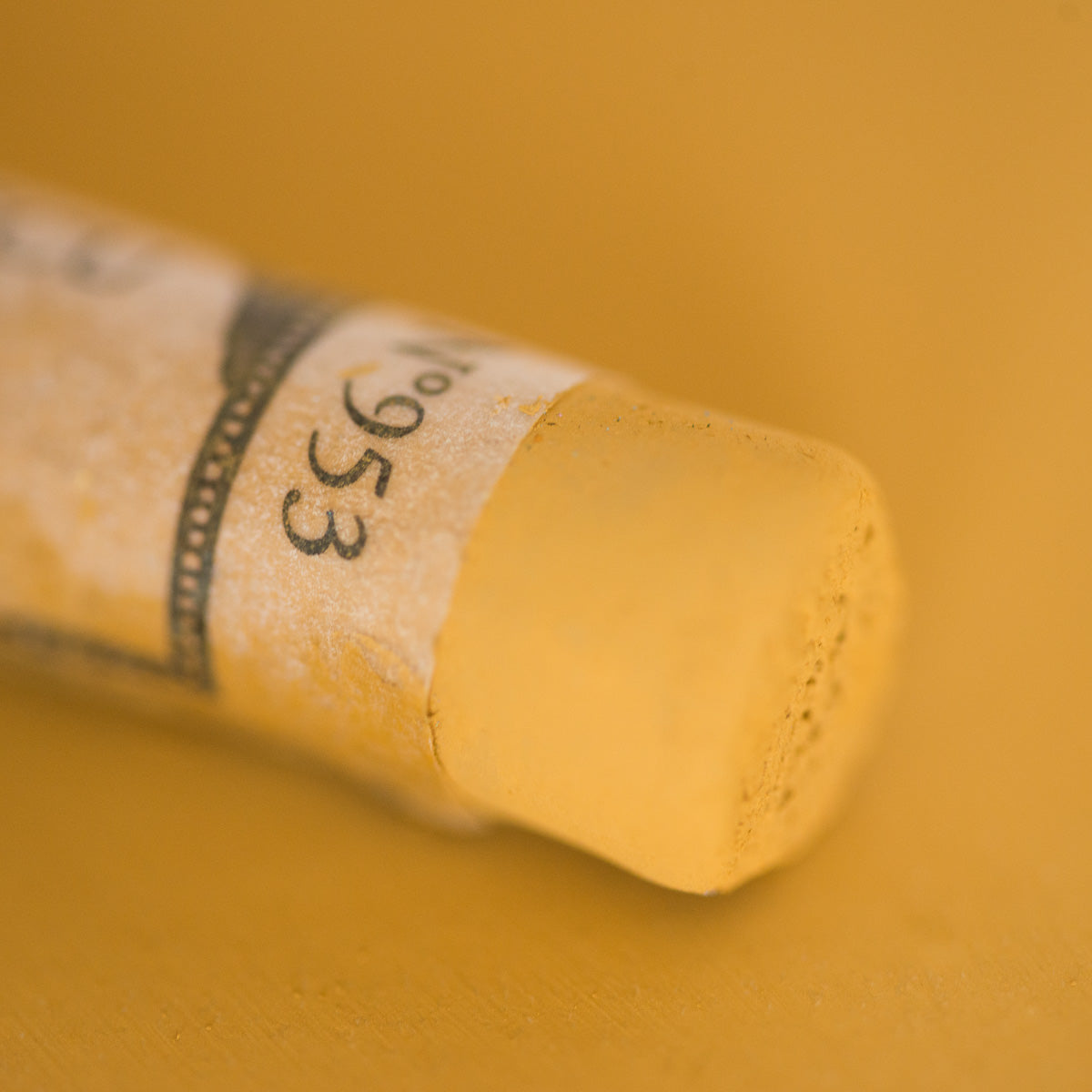 A close-up of a yellow Sennelier extra soft pastel. on the same coloured background, with the colour information printed on the paper wrap.