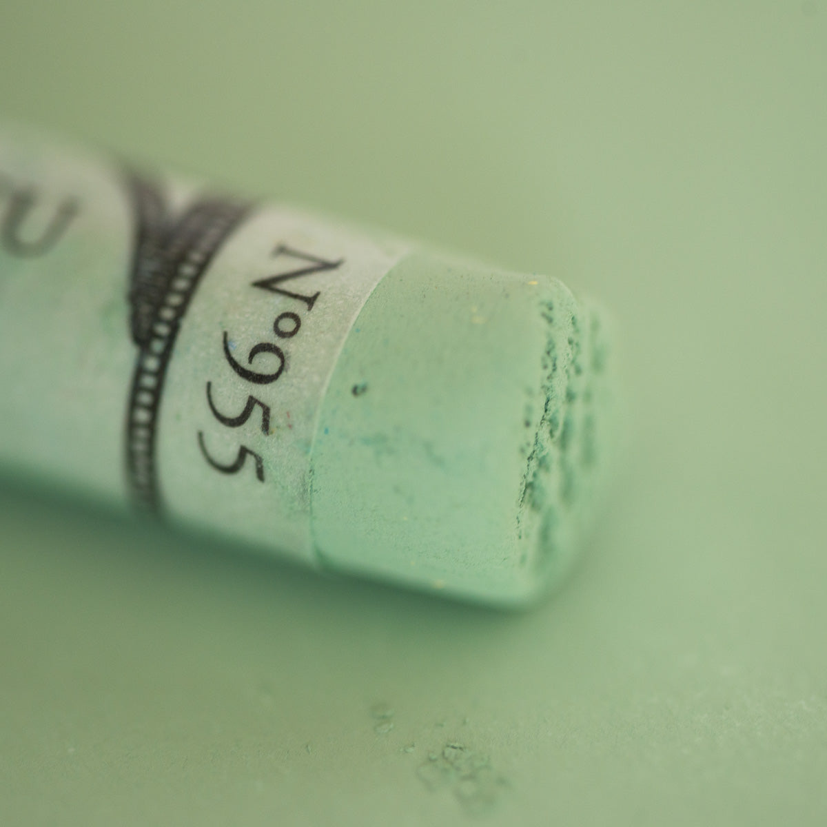 A close-up of a light green Sennelier extra soft pastel. on the same coloured background, with the colour information printed on the paper wrap.