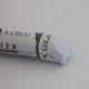 A close-up of a white Sennelier extra soft pastel on the same coloured background, with the colour information printed on the paper wrap.